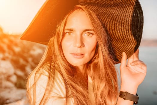 Portrait of happy young woman wearing summer black hat with large brim at beach on sunset. Closeup face of attractive girl with black straw hat. Happy young woman smiling and looking at camera at sea