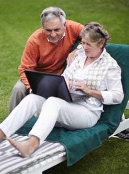 Retirement, laptop and an old couple in the garden of a hotel for travel or vacation at a luxury resort. Love, technology or social media with a senior man and woman tourist on a deckchair at a lodge.