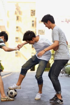 Friends in city street playing soccer together for sports, fun and happy energy with urban games in Korea. Ball game for teen friendship, group of people in road with football, weekend in community