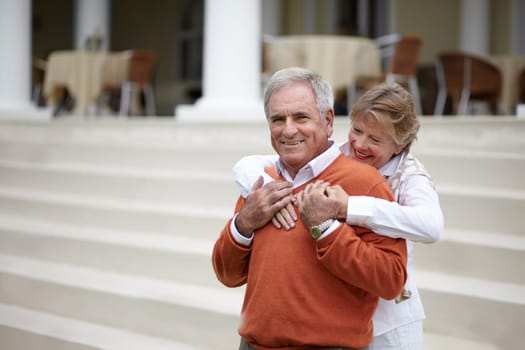 Hug, hospitality and an old couple on hotel steps for travel, vacation or tourism in luxury accommodation. Love, relax or retirement with a senior man and woman hugging on the staircase of a resort.