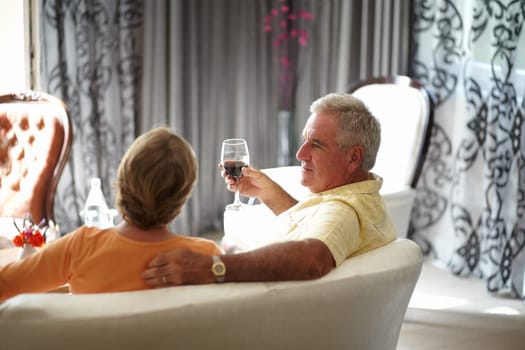 Retirement, sofa and an old couple drinking wine in their hotel room while on holiday or vacation together. Toast, love or relax with a senior man and woman bonding at a luxury resort for romance.