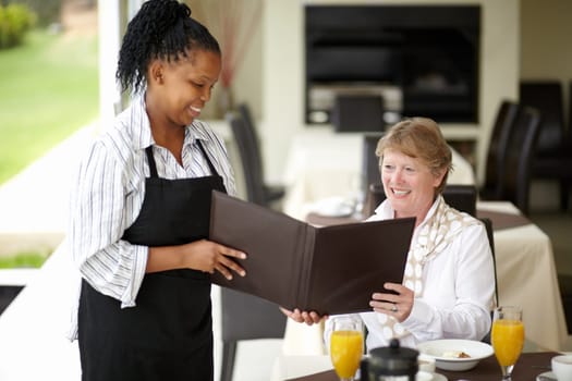 Waitress, service and senior woman in a restaurant for breakfast or lunch at a hotel with a menu and choice of food. Friendly, order and elderly person happy on vacation or holiday for hospitality.