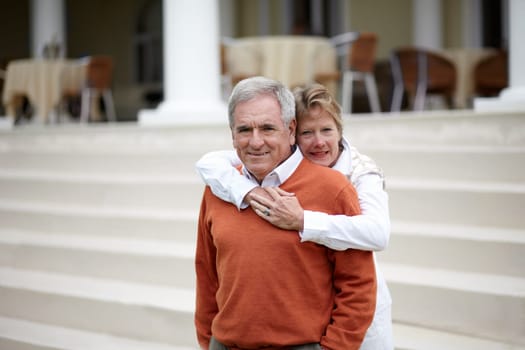Hug, portrait and an old couple on hotel steps for travel, vacation or tourism in luxury accommodation. Love, retirement or hospitality with a senior man and woman hugging on a resort staircase.