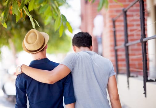 City, travel and back of gay couple walking together in the street while on a tourism vacation. Love, affection and male friends embracing in an outdoor urban road while on a weekend trip or holiday