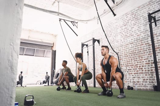 Focus on every single rep. a fitness group holding kettlebells while doing squats at the gym