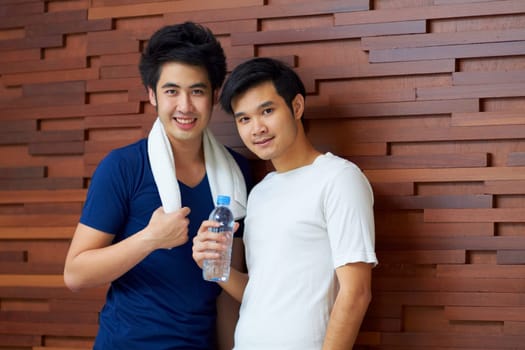 Happy, portrait and gay couple at the gym with water on a break from a workout together. Smile, wellness and Asian lgbt men training at a club for exercise, health and happiness with fitness.