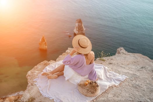 woman sea travel. photo of a beautiful woman with long blond hair in a pink shirt and denim shorts and a hat having a picnic on a hill overlooking the sea.