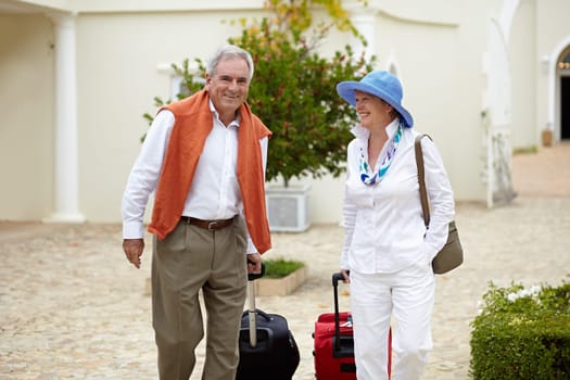 Travel, suitcase and elderly couple walking on vacation in a holiday location happy in retirement together by a hotel. Bag, smile and senior people on a journey or man and woman walk in happiness.