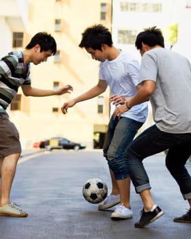 Friends in street playing football together for sports, fun and happy energy with urban games in Korea. Games for kids, friendship and teen group in road with soccer ball, weekend time in Asian city