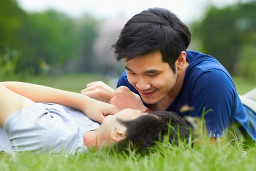 Asian men, gay couple and lying in park, grass or garden with love, care and bonding with kiss in summer. Happy Japanese guy, romantic and relax together on lawn for lgbtq, smile, outdoor in nature.