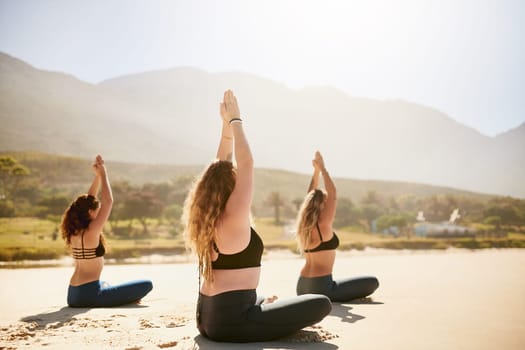 Yoga is liberating. Rearview shot of three young women practising yoga on the beach