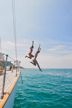 Summer, sailing and friends jumping off a yacht together into the ocean for freedom, fun or swimming. Travel, energy and bikini with girls leaving a boat to jump into the sea while on a luxury cruise.