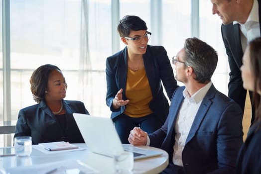 Diversity, colleagues with laptop and at desk in a boardroom of their modern workplace. Collaboration or teamwork, support or brainstorming for help and coworkers working together on a project.