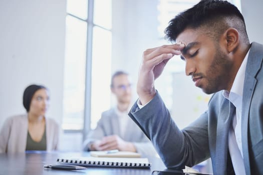 Mental health, businessman with a headache and at a business meeting with colleagues in a boardroom office at their workplace. Stress or depression, anxiety or tired and sad male person at a desk.