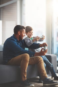 This is our most favorite game. a cheerful little boy and his father playing video games together on the television while being seated on the sofa at home during the day