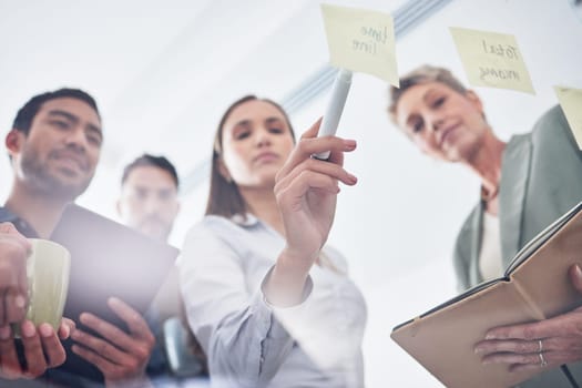 Teamwork, writing and business people on glass board for planning, brainstorming and schedule or workflow notes. Notebook, tablet and women, men or group with sticky note ideas, solution and window.