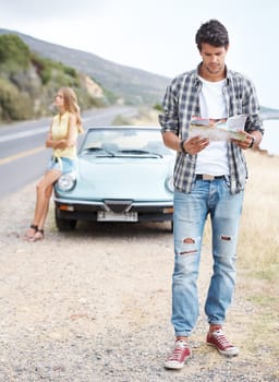 Trying to find the right route. Handsome young guy trying to find his way on a roadtrip while his girlfriend looks on in annoyance