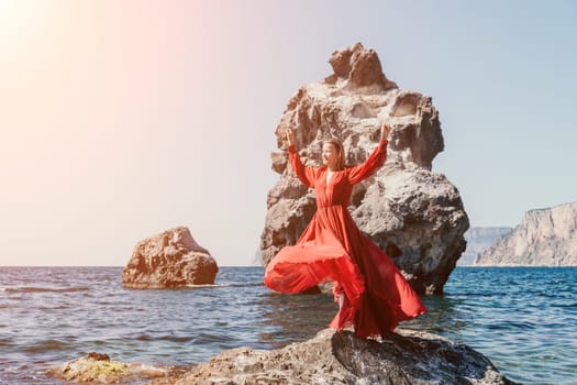 Woman travel sea. Young Happy woman in a long red dress posing on a beach near the sea on background of volcanic rocks, like in Iceland, sharing travel adventure journey