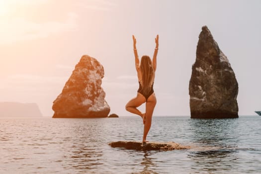 Woman meditating in yoga pose silhouette at the ocean, beach and rock mountains. Motivation and inspirational fit and exercising. Healthy lifestyle outdoors in nature, fitness concept.