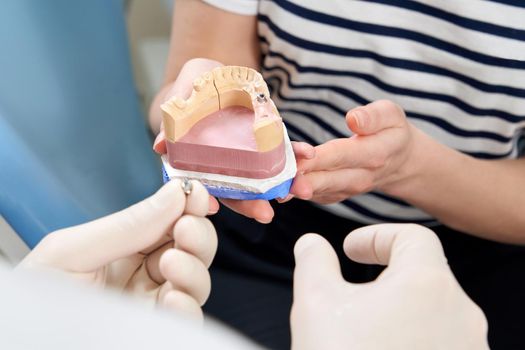 Male dentist showing his female patient a dental implant in modern clinic