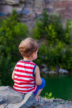 A child sits on the top of a beautiful canyon and looks at the water in it. The bank of the canyon. Portrait of a child.