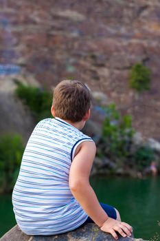 A child sits on the top of a beautiful canyon and looks at the water in it. The bank of the canyon. Portrait of a child.