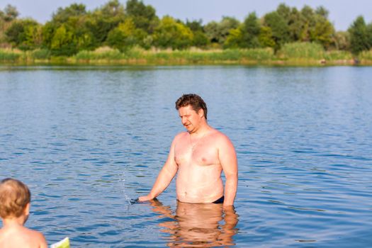 A family, a father and his sons are swimming in the river on a very hot summer day. Swim in reservoirs. A happy family has fun and splashes in the water in the summer. Family on vacation