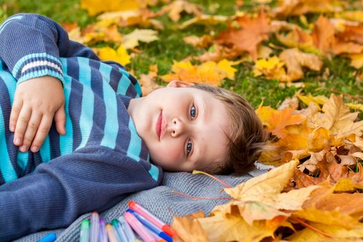 Autumn mood. The boy is thoughtfully drawing something in his notebook.Autumn portrait of a child in yellow foliage. Sight. A sweet, caring boy. Autumn