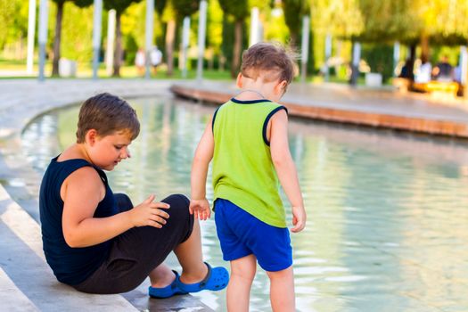 Children in the park dip their feet in the fountain they are very happy. Have fun and rejoice on a summer day at the fountain. Walking in the park