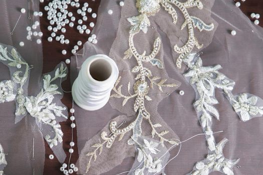 close-up of female hands of seamstress tailor sewing wedding dress using beads and lace in the studio