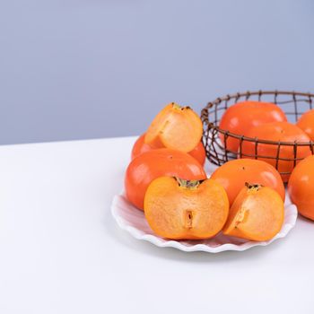 Fresh beautiful sliced sweet persimmon kaki isolated on white kitchen table with gray blue background, Chinese lunar new year design concept, close up.