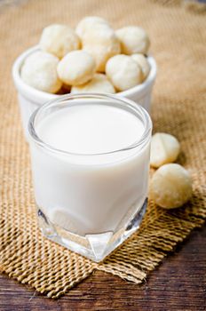 Macadamia milk in a glass and a bowl of macadamia nuts on a wooden background.