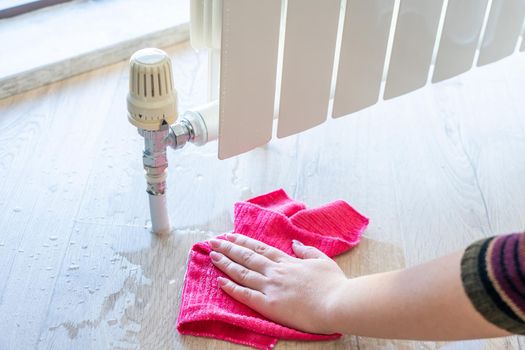 Female hand with rag cleaning water from heating radiator