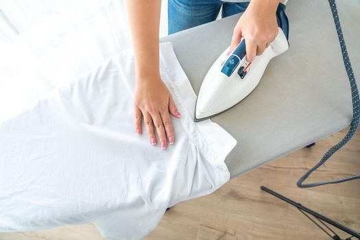 Close up of Female hands ironing white shirt on ironing board