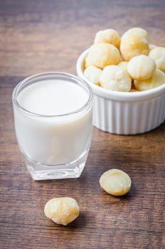 Macadamia milk in a glass and a bowl of macadamia nuts on a wooden background.