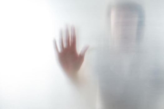 Diffused silhouette of female hands through frosted glass