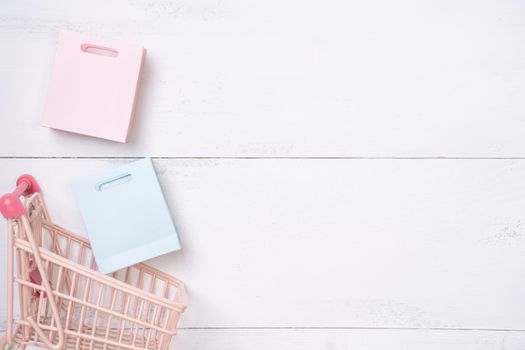 Abstract design element,annual sale,shopping season concept,mini cart with colorful paper bag on white wooden table background,top view,flat lay