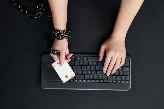 Woman with metal chain holding credit card over keyboard, online buying addiction concept