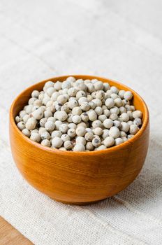 Dried white peppercorn seeds in wooden cup.