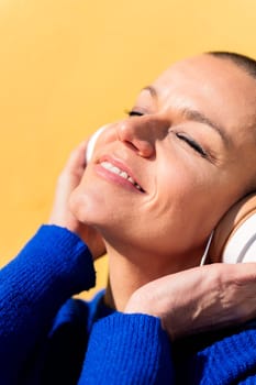 happy woman enjoying music on headphones on yellow background, concept of rhythm and positive people, copy space for text