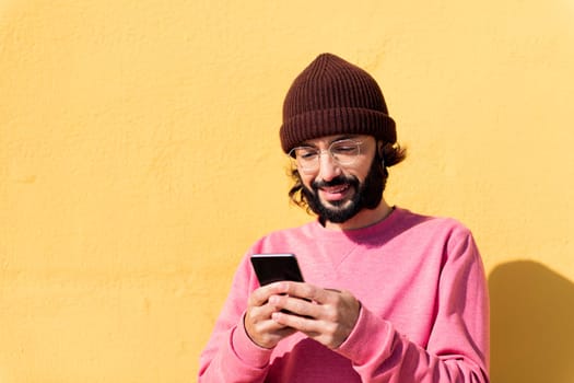smiling young man using mobile phone in a yellow background, concept of technology of communication and modern lifestyle, copy space for text