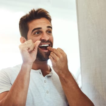 Dental floss, morning and teeth with man in bathroom mirror for cleaning, habit and oral hygiene. Smile, cosmetics and health with male person flossing at home for self care, breath and mouth.