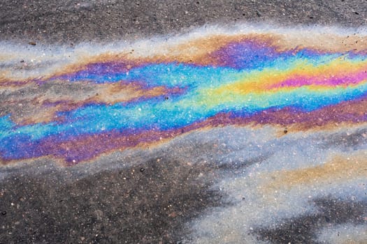 Petroleum fuel spilled on wet asphalt, abstract background.