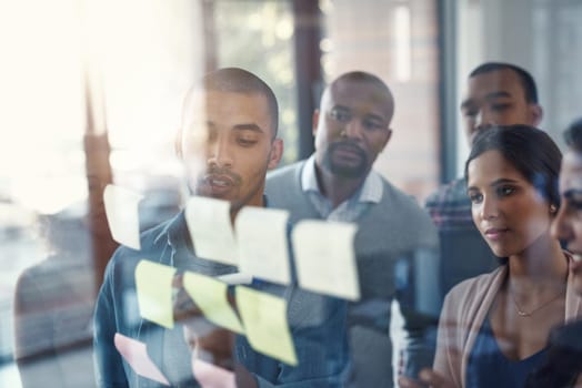 Teamwork is the best way to achieve success. High angle shot of a group of coworkers brainstorming on a glass wall