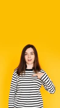 Delighted Woman Pointing at Herself in Amazement - Humorous Reaction Concept on Bright Yellow Background. Surprised and Amused Woman Pointing at Herself with Open Mouth - Self-Recognition Humor.
