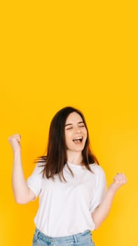 Exultant Woman Celebrating with Fist Raised, Shouting 'Yes' - Victory, Achievement, Success Concept on Vibrant Yellow Background.