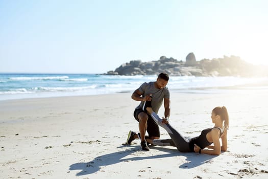Getting through their warmup routine. a sporty young couple stretching while exercising along the beach