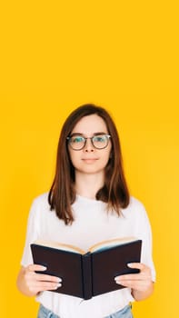 Joyful Student immersed in Reading: Cheerful Woman with Glasses Enjoying a Novel Book - Education and Leisure Concept Isolated on Vibrant Yellow Background