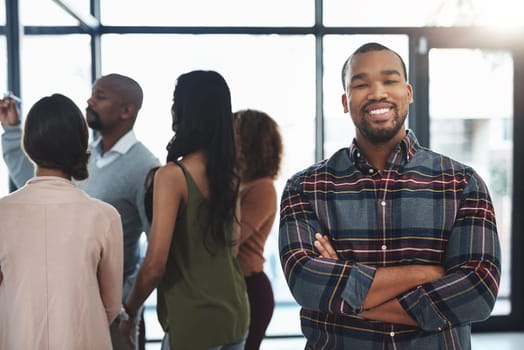 Im confident in my team. Portrait of a handsome young man standing in the office with his colleagues in the background