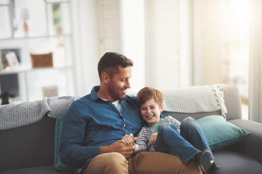 Okay you win dad. a cheerful little boy and his father playing around together while being seated on a sofa together at home